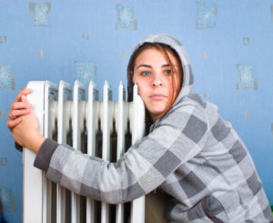 girl hugs a water filled radiator inside her house trying to keep warm